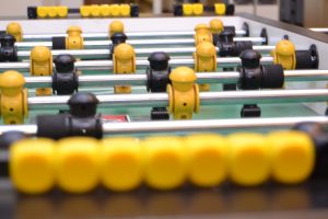 Close-up of a foosball table with rows of yellow and black players attached to metal rods, with a green surface mimicking a soccer field.