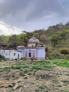 An old shrine surrounded by greenery and trees against a cloudy sky.