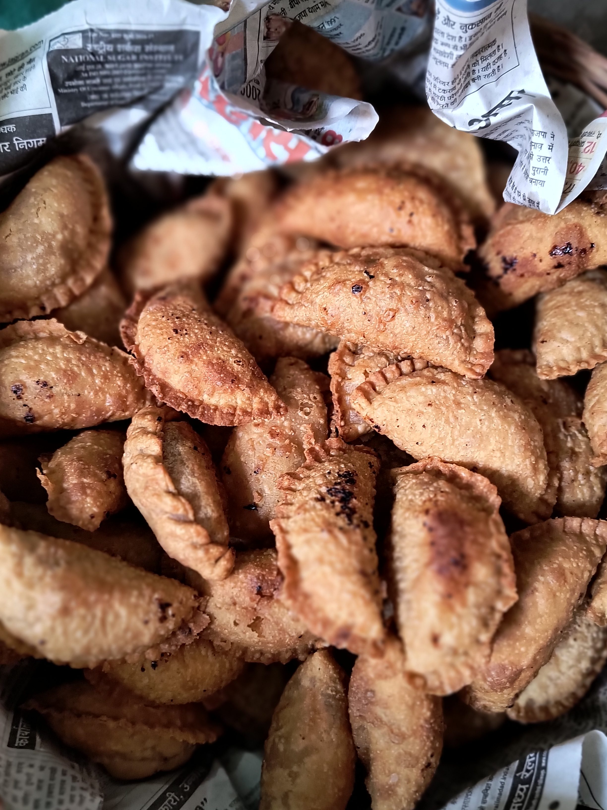 A basket filled with golden-brown Gujhia, a traditional sweet made in India, especially for the occasion of Holi, wrapped in newspaper.