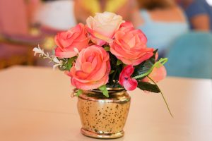 A bouquet of artificial pink and peach roses arranged in a golden vase on a table 