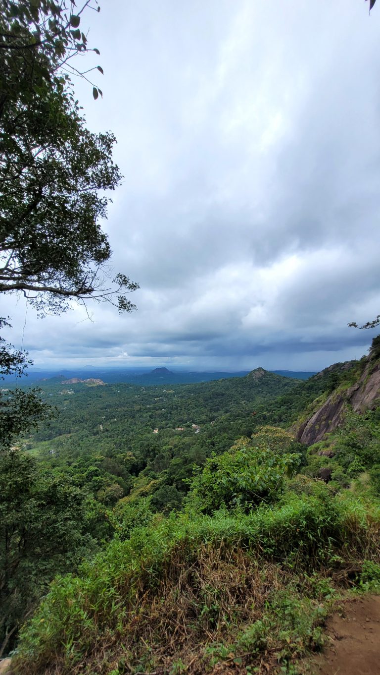 Lush green landscape view from a mountain over the edakkal cave with a cloudy sky above and hills in the distance.