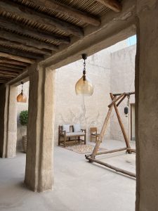 Two glass pendant lights hang from the ceiling. The courtyard features wooden outdoor furniture, including a bench with two cushions and a small chair