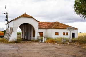 An abandoned customs office at the Spain-Portugal border, showcasing a white building with a red tile roof. Sealed windows and a stone sign saying "Portugal