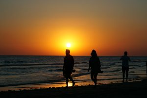 Three silhouetted people walking along the shoreline with waves coming in at sunset.