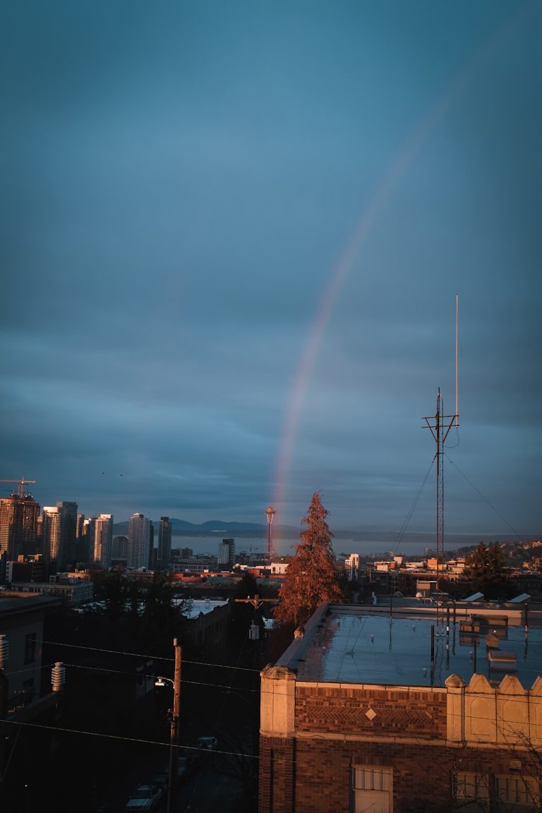 Zoomed out view of a rainbow hitting the Seattle space needle against a moody, rainy day