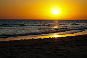 A scenic sunset view over the ocean, with the golden sun reflecting on the water and a clear sky above the horizon, as viewed from a sandy beach in the south of spain.
