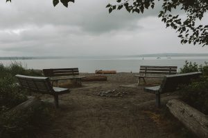 View larger photo: Set of four benches in a circle on a beach with views of the ocean in the background, along with several boats. 