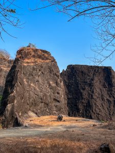 A rugged landscape with a large rock formation and a motorcycle parked at the base of the rocks.