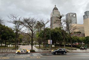 A park in Taipei with a road and cars in the foreground, and high-rise buildings in the background.
