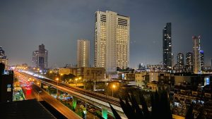 Night view of a high-rise building with a metro bridge illuminated against the dark sky.