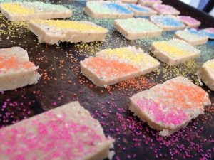 sheet of shortbread cookies going in to the oven. they have colored sugar on top of them in a diagonal rainbow pattern