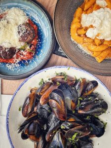 A trio of dishes: mussels garnished with parsley, meatballs in tomato sauce topped with cheese, and pasta with ricotta and tomato sauce.






