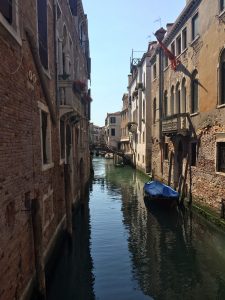 A lone, covered gondola docked on Rio dei Mendicanti between opposing two story brick buildings (Venice, Italy)
