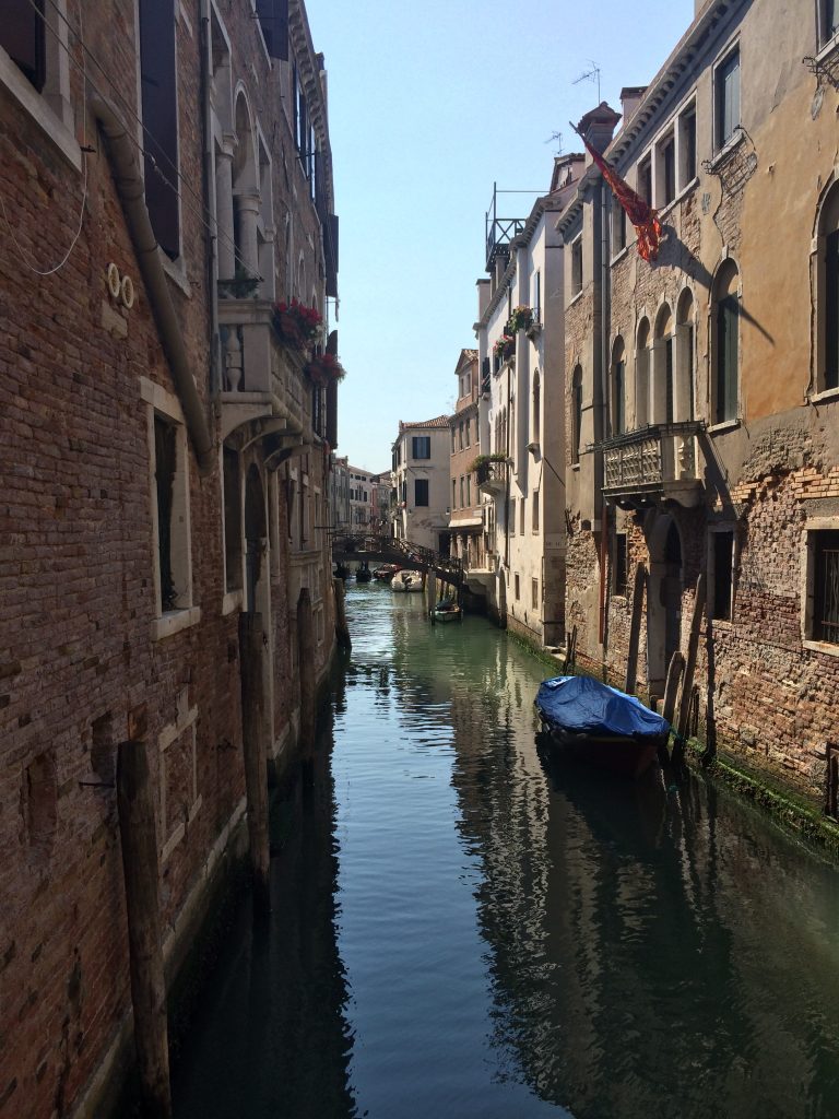 A lone, covered gondola docked on Rio dei Mendicanti between opposing two story brick buildings (Venice, Italy)