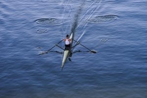 A women in a single scull rowing around the boat on the Guadalquivir river.
