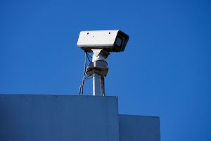 Security camera on top a blue building with a deep blue sky behind