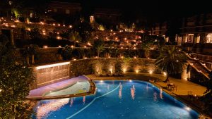 A peaceful nighttime poolside scene with rich greenery and subtle lighting enhancing the natural beauty.