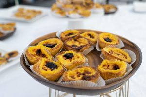 A tray of Portuguese pastries, known as Pastéis de nata, displayed on a white table with other food.