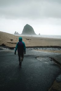 Person walking down a path towards a sandy shore in front of Haystack Rock in Cannon Beach, Oregon, USA.