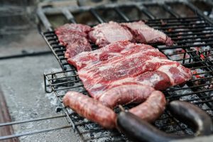 Raw steaks and sausages on a barbecue grill over glowing coals.