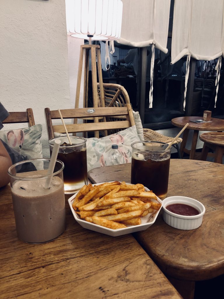 On the table are two glasses of iced coffee, a chocolate shake with a straw, a plate of seasoned French fries, and a small cup of ketchup.