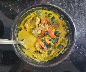 一种传统的喀拉拉邦咖喱鱼，配番茄和椰奶，放在厨房柜台上，用汤匙盛在黑锅里。
