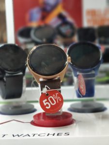 A display of smartwatches, with the central watch featuring a gold bezel and leather strap, prominently tagged with a red “50%” discount sign. Several other smartwatches are in the background, also marked with similar discount tags.
