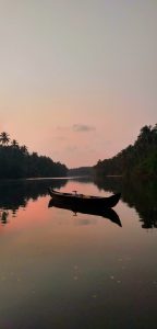 View larger photo: A serene sunset scene with a wooden canoe moored on a calm river, surrounded by lush tropical foliage reflecting on the water's surface.