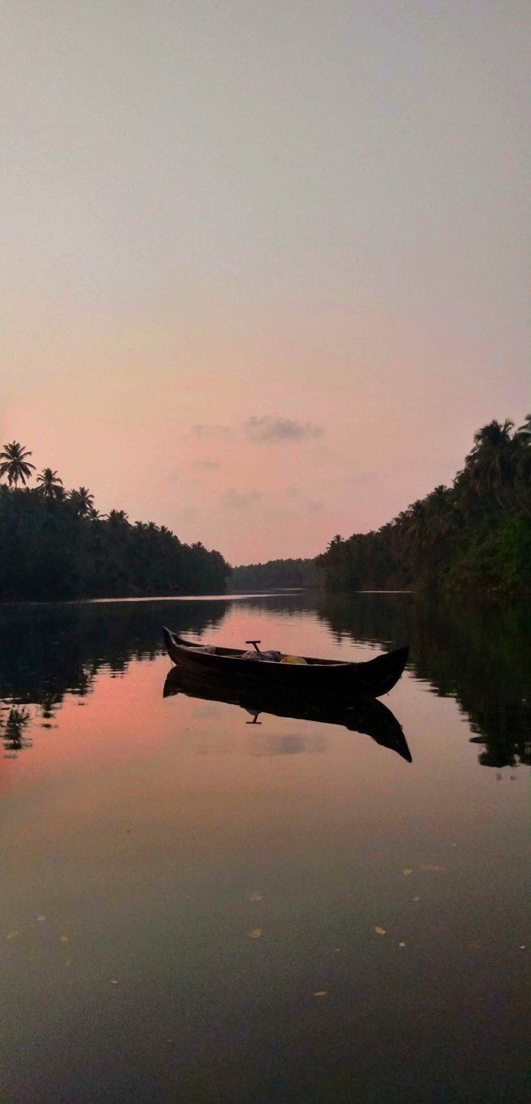 A serene sunset scene with a wooden canoe moored on a calm river, surrounded by lush tropical foliage reflecting on the water’s surface.