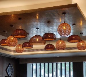 The ceiling of a dining space is adorned with a captivating array of wooden and bamboo lights, casting a warm, ambient glow. The intricate craftsmanship and natural materials create an inviting atmosphere that perfectly complements the rustic charm of the space.