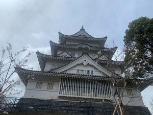 A Japanese castle with multiple tiers and a cloudy sky in the background, partially obscured by blossoming cherry trees on each side.
千葉県千葉市中央区　亥鼻公園　天守閣風展望台　/　Inahana Park, Chuo-ku, Chiba City, Chiba Prefecture Keep-style observatory