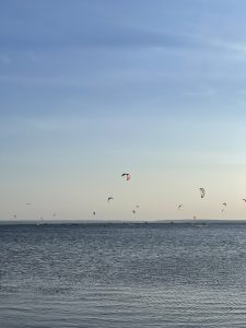 A serene seascape at dusk, with the calm waters of the sea extending to the horizon under a clear blue sky, dotted with colorful kites