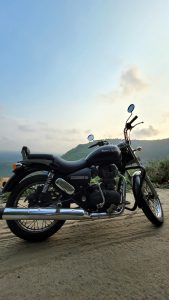 Side view of a Royal Enfield motorcycle in a dirt road in from of a valley at sunset
