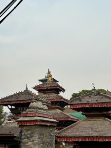 Traditional Nepalese pagoda-style temples with tiered roofs and elaborate finials, under a hazy sky with power lines in the foreground at world heritage site Basantapur Durbar Square Nepal.

