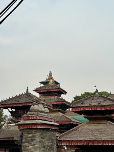 Traditional Nepalese pagoda-style temples with tiered roofs and elaborate finials, under a hazy sky with power lines in the foreground at world heritage site Basantapur Durbar Square Nepal.