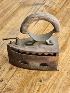 A vintage cast iron coal iron with a wooden handle on a rustic wooden surface. 