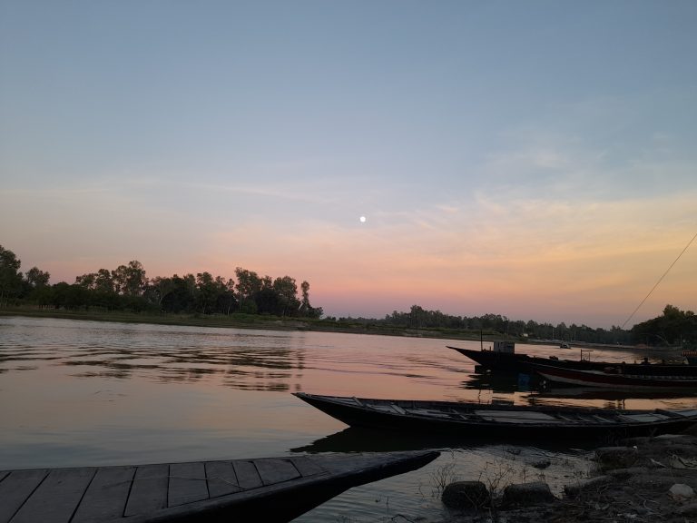 A peaceful riverside at sunset with Three wooden boats docked along the shore