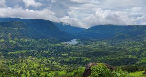 A scenic view of a lush green valley surrounded by mountains under a cloudy sky