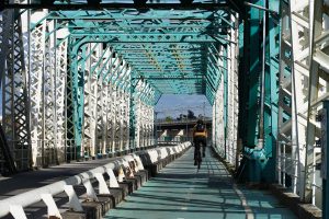 Man riding his bicycle on the bike line of an old white and green iron bridge