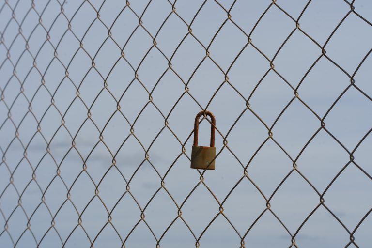 A small rusty padlock on a wire fence.