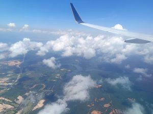 Blue sky view from an aircraft with numerous groups of white clouds. Tiny boats are drifting across the river.

