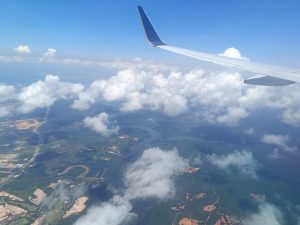  Blue sky view from an aircraft with numerous groups of white clouds. Tiny boats are drifting across the river.
