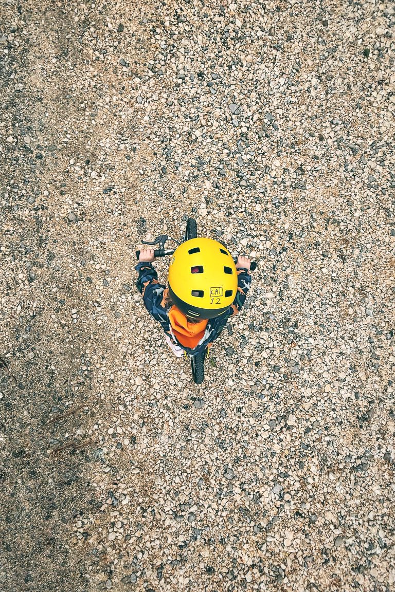 Kid on bike with yellow helmet on gravel, bird-eye view