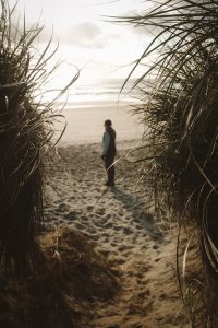 View larger photo: View between a sandbank of a person looking out onto a beach.