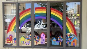 Five panel window storefront painted with a colorful house, tree, and car neighborhood design with a large rainbow arching over it all 