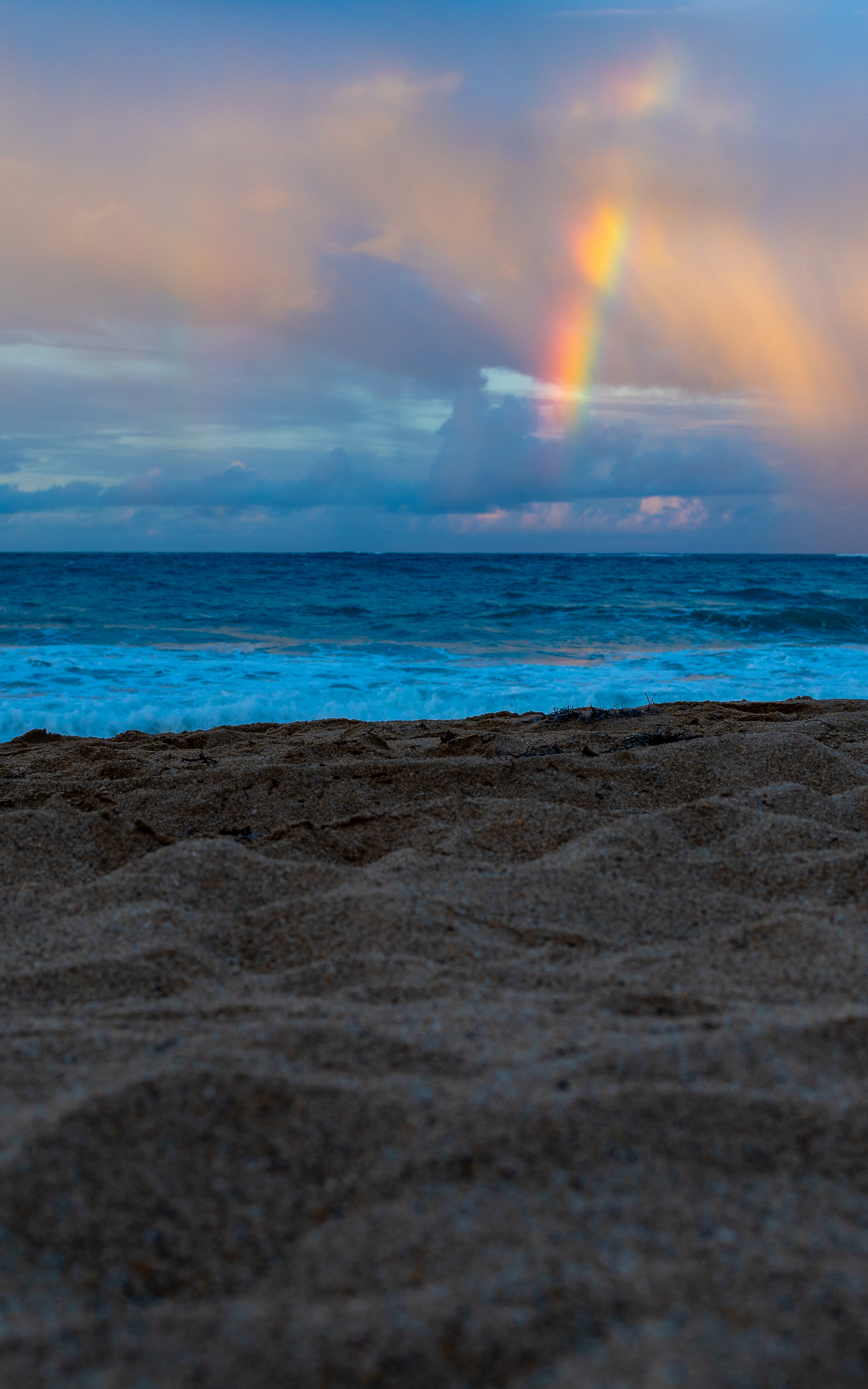 A rainbow above the ocean with a sandy beach in the foreground.
