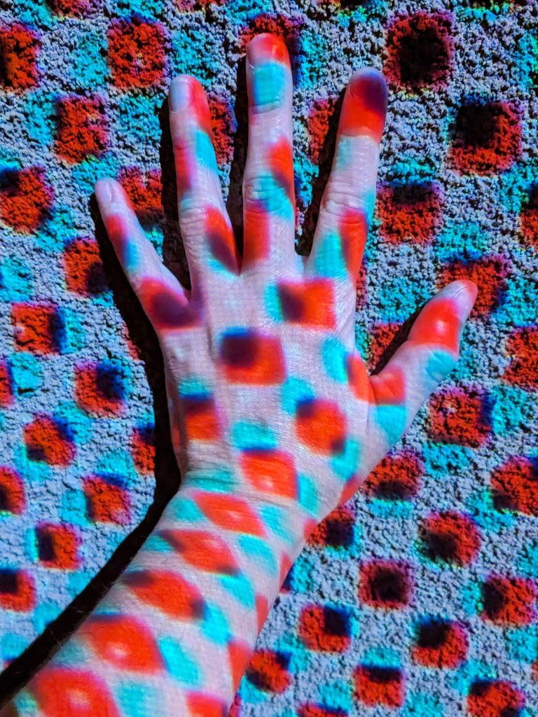 A hand against the wall with blue and red light dots.