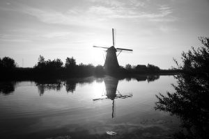 Black and white photo of a canal in front of a windmill at Kinderdijk, The Netherlands. (UNESCO heritage)
