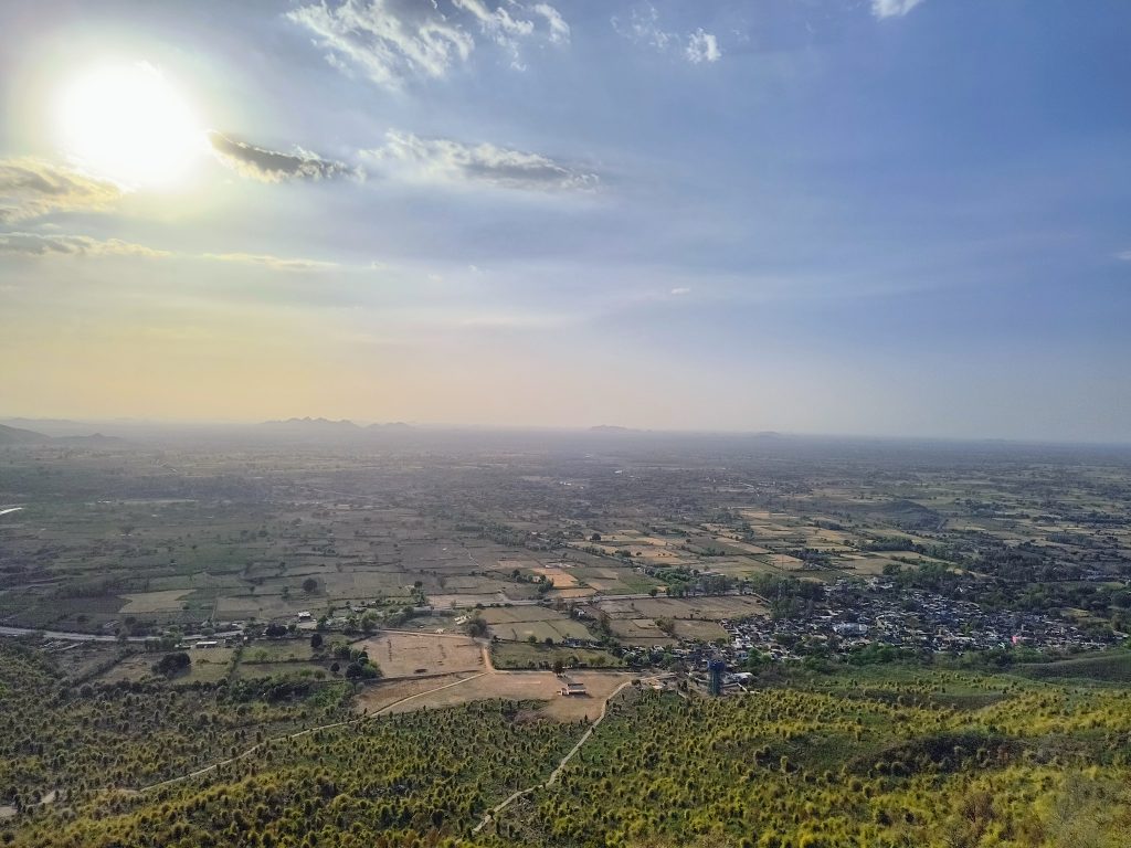 A panoramic view from Kalinjar Fort, showing expansive farmlands and distant hills under a setting s...