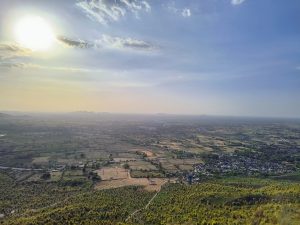 A panoramic view from Kalinjar Fort, showing expansive farmlands and distant hills under a setting sun, bathed in warm light.